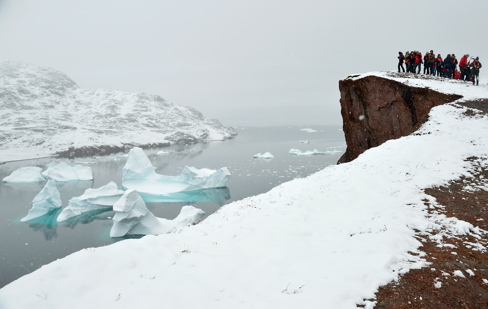 Wandergruppe auf einer Klippe über einem eisbedeckten Fjord im Scoresby Sund