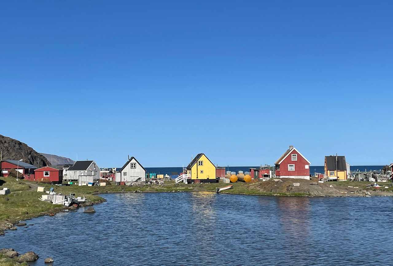 Bunte Holzhäuser eines grönländischen Dorfes am Wasser bei Sonnenschein