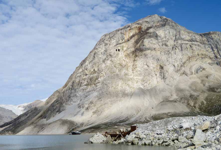 Heller Marmorfelsen über dem Fjord mit dunklen Stolleneingängen, davor die MS Cape Race