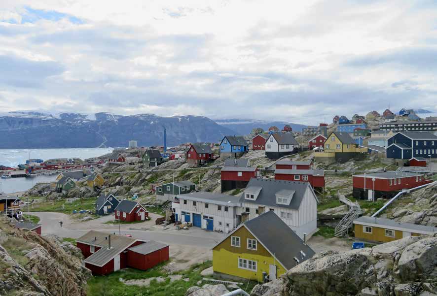 Der Ort Uummannaq mit bunten Häusern auf Felsgrund, dahinter Fjord und Berge