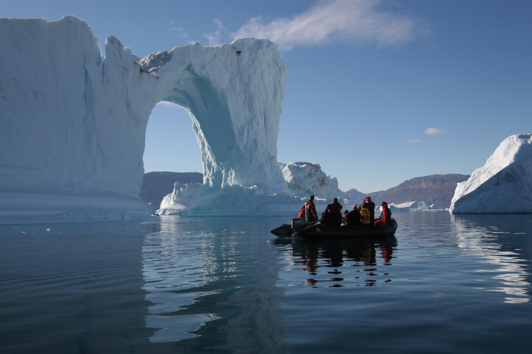 Zodiac mit Gästen vor einem großen Eisbogen im Scoresby Sund