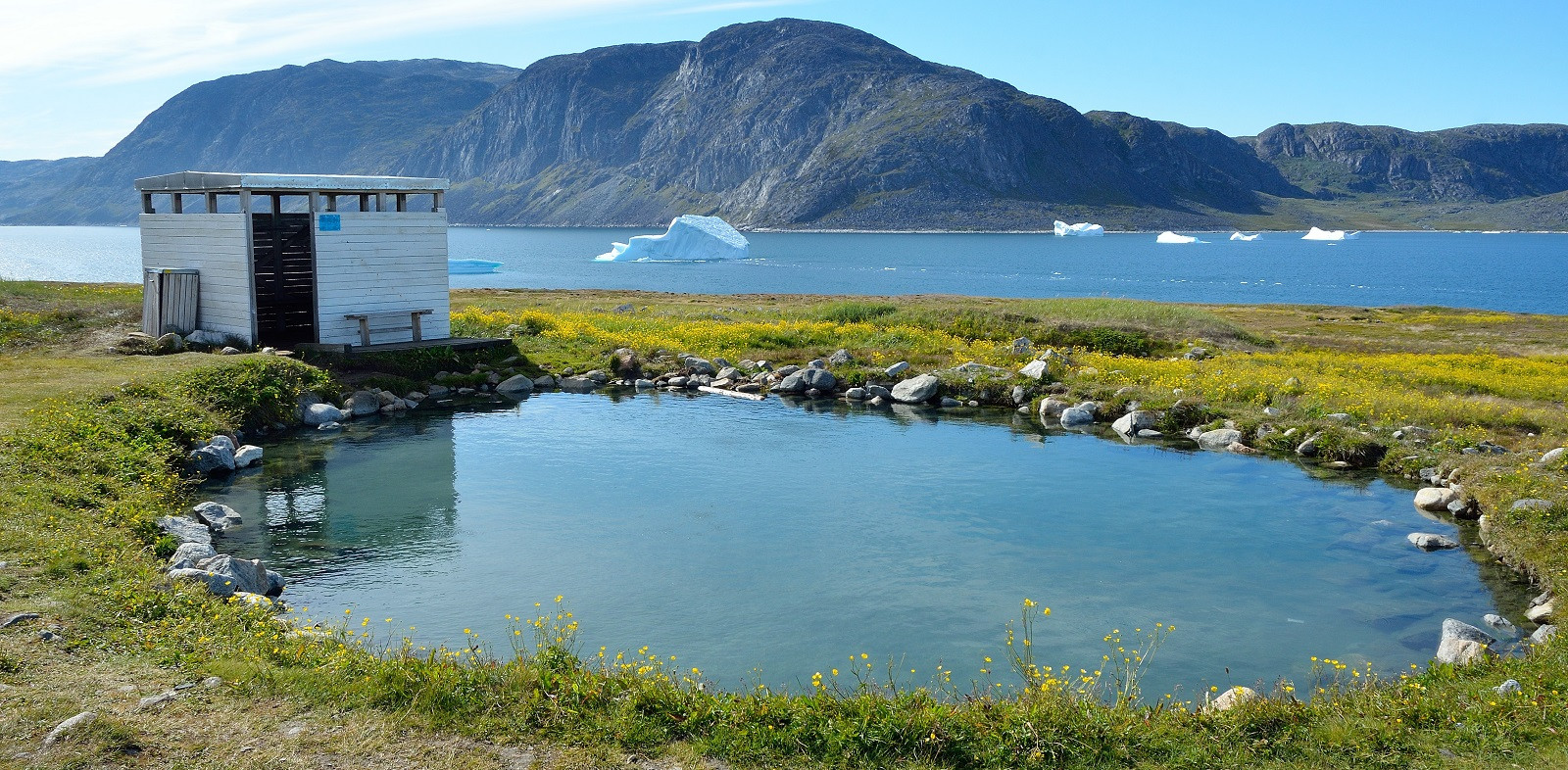 Heiße Quelle von Unnartoq in Südgrönland, dahinter Eisberge im Fjord